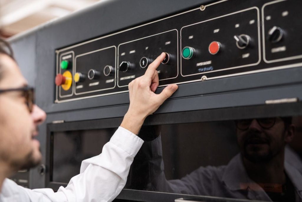 Over shoulder view of young operator pushing button on control panel while working in automated industry