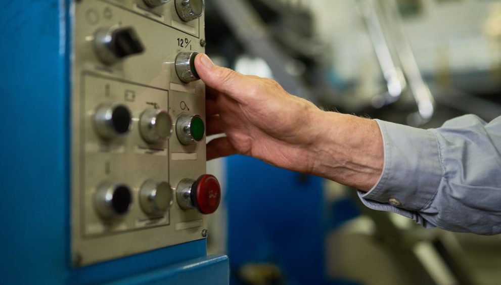 Closeup of unrecognizable senior worker operating machines in factory, hands pressing buttons on control panel