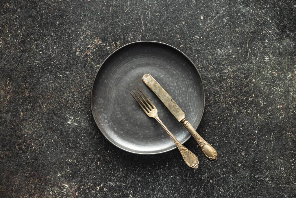 Empty vintage plate with silver knife and fork on black table.  Top view.