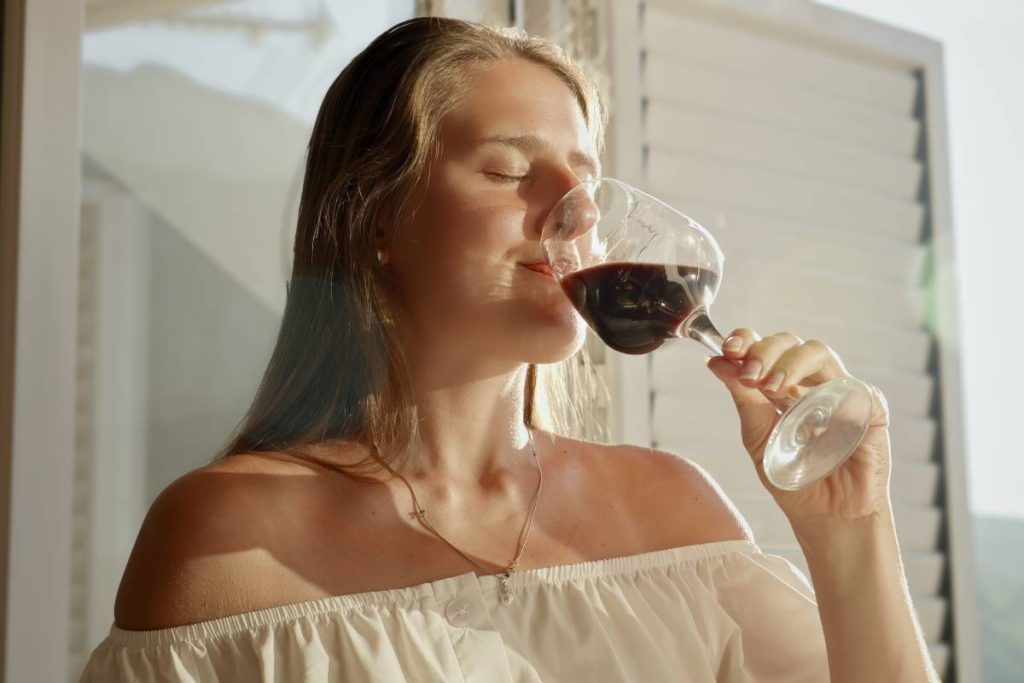 Closeup portrait of young woman with closed eyes enjoying taste of red wine in sunset light.