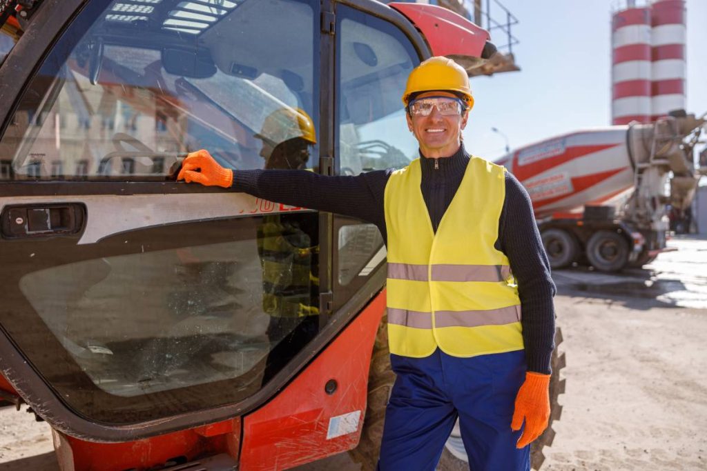 Joyful male worker in safety helmet looking at camera and smiling while placing hand on truck