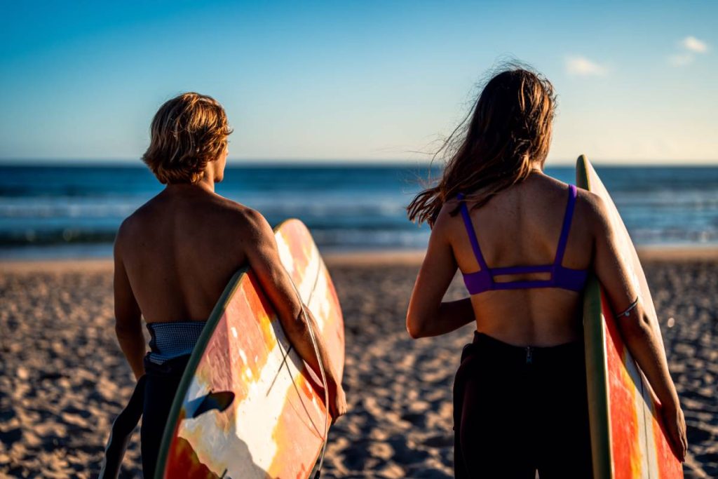 Two surfers prepares to hit the waves as they standing on the beach with their surfboards at surf camp australia.