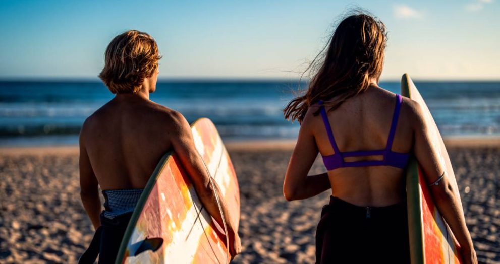 Two surfers prepares to hit the waves as they standing on the beach with their surfboards at surf camp australia.