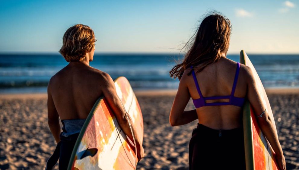 Two surfers prepares to hit the waves as they standing on the beach with their surfboards at surf camp australia.