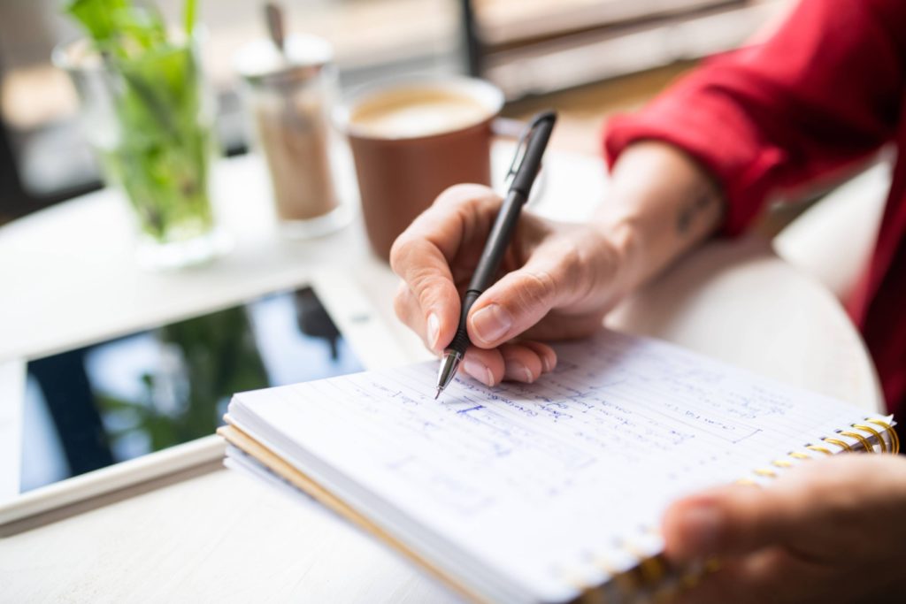 Hand of young businesswoman with pen making notes on page of notebook