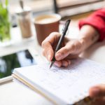 Hand of young businesswoman with pen making notes on page of notebook