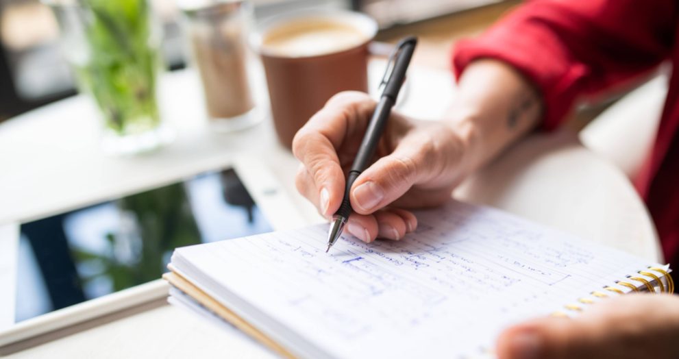 Hand of young businesswoman with pen making notes on page of notebook