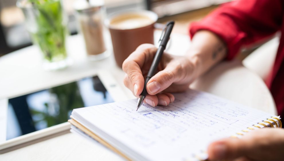 Hand of young businesswoman with pen making notes on page of notebook