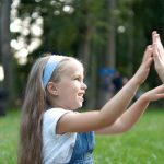 Pretty little child girl playing game with her mom clapping their hands together outdoors in green summer park.