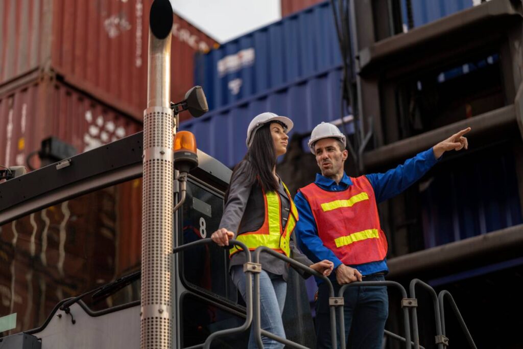 Two logistics workers man and woman discuss operations at a busy shipping container yard. successful coordination in freight, transportation, and supply chain operations