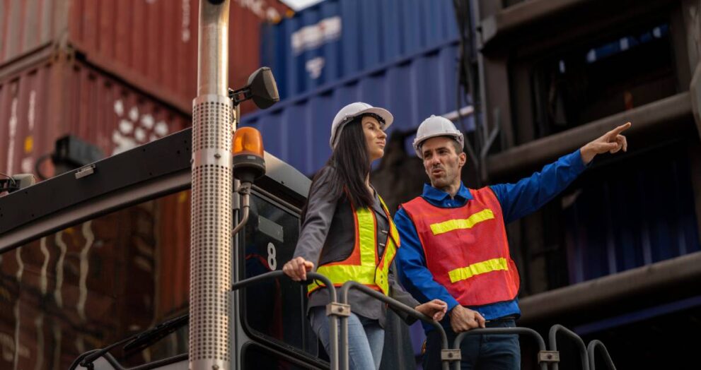 Two logistics workers man and woman discuss operations at a busy shipping container yard. successful coordination in freight, transportation, and supply chain operations