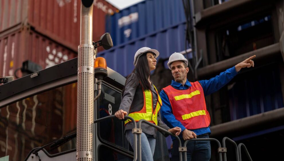 Two logistics workers man and woman discuss operations at a busy shipping container yard. successful coordination in freight, transportation, and supply chain operations