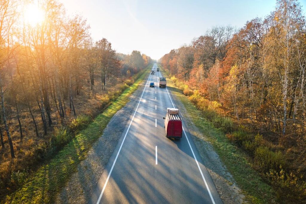 Aerial view of intercity road with fast driving cars between autumn forest trees at sunset. Top view from drone of highway traffic in evening.