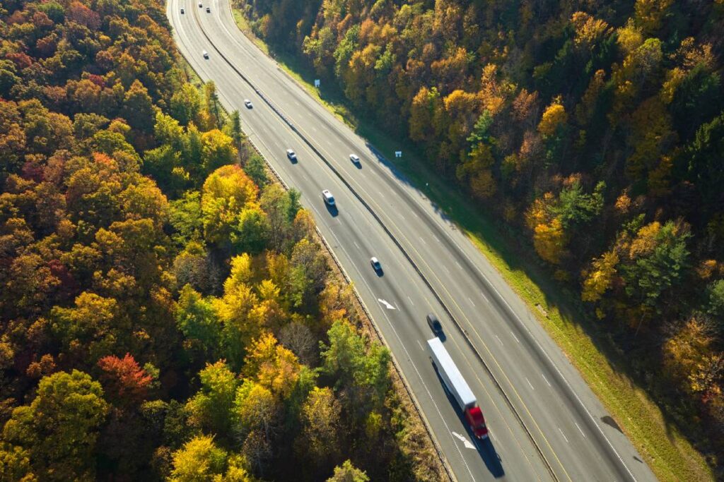 I-40 freeway road leading to Asheville in North Carolina over Appalachian mountain pass with yellow fall forest and fast moving trucks and cars. Concept of high speed interstate transportation.