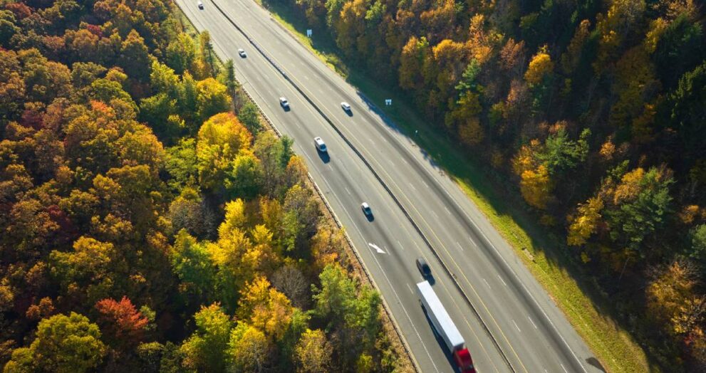 I-40 freeway road leading to Asheville in North Carolina over Appalachian mountain pass with yellow fall forest and fast moving trucks and cars. Concept of high speed interstate transportation.