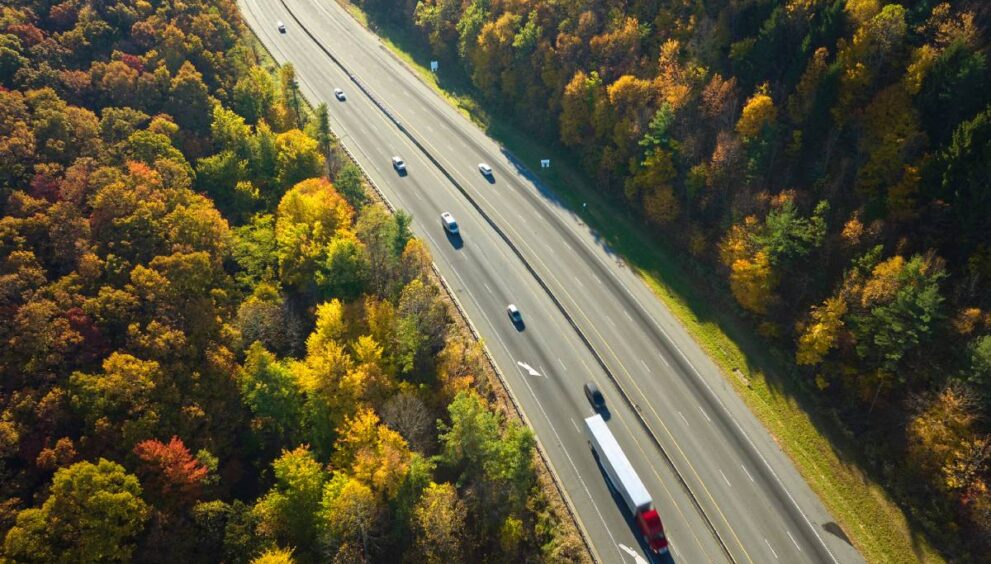 I-40 freeway road leading to Asheville in North Carolina over Appalachian mountain pass with yellow fall forest and fast moving trucks and cars. Concept of high speed interstate transportation.